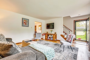A spacious living room with a sofa, armchair, and a coffee table. There's a television mounted on the wall and a wooden cabinet with decorative items. - 11 Mi to Dtwn Columbus: Peaceful Townhome w/ Yard! (Columbus)
