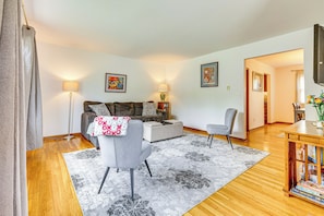 A living room with a sofa, armchair, and coffee table, a wooden floor, and a bookshelf with books. - 11 Mi to Dtwn Columbus: Peaceful Townhome w/ Yard! (Columbus)