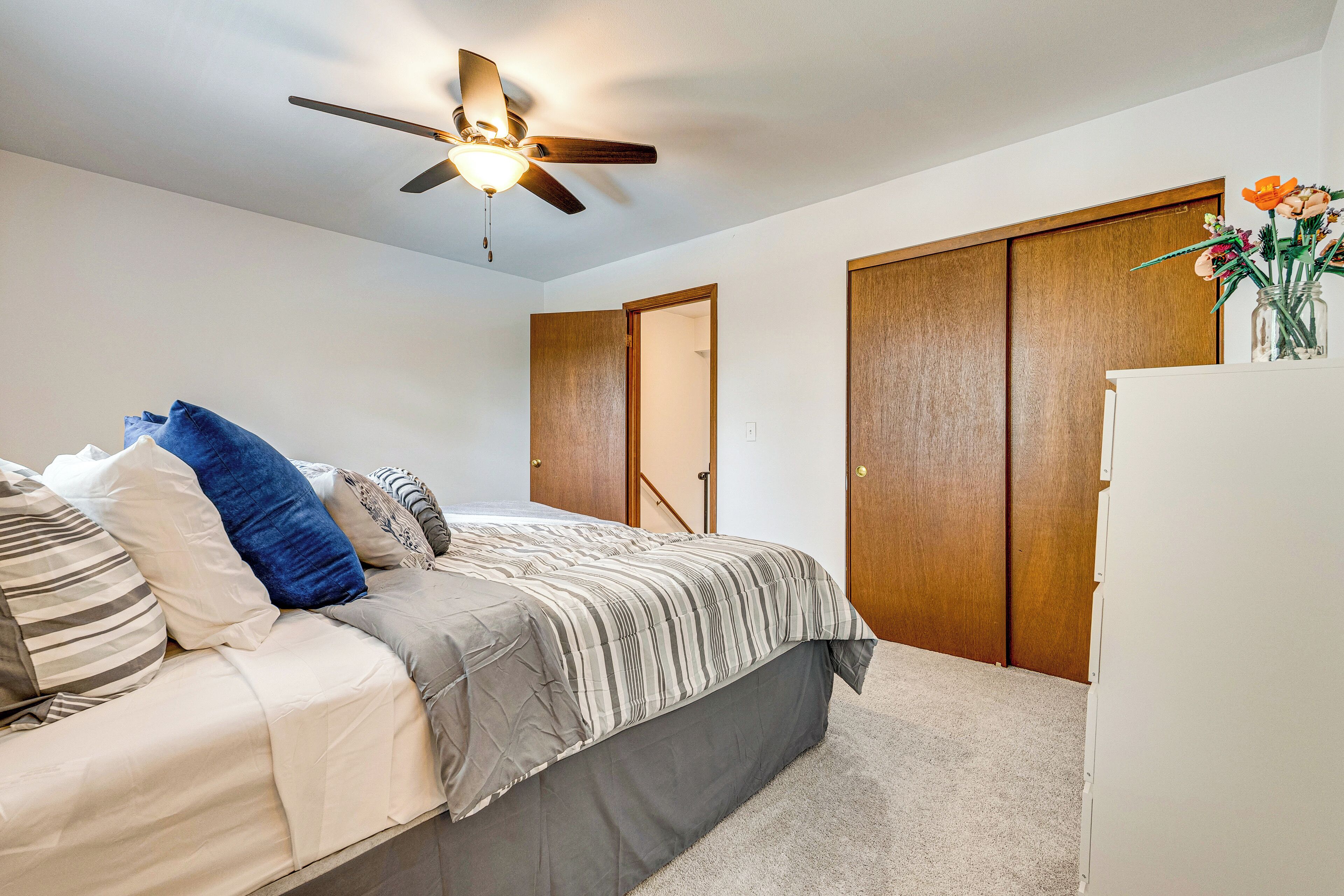 Ein Schlafzimmer mit Bett, Deckenventilator, Kleiderschrank und Kommode.
