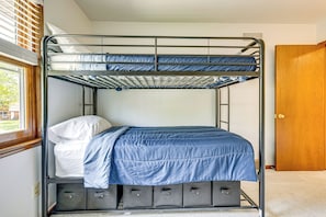 Un lit superposé avec un matelas bleu et des oreillers blancs, une porte en bois et une fenêtre avec des stores.