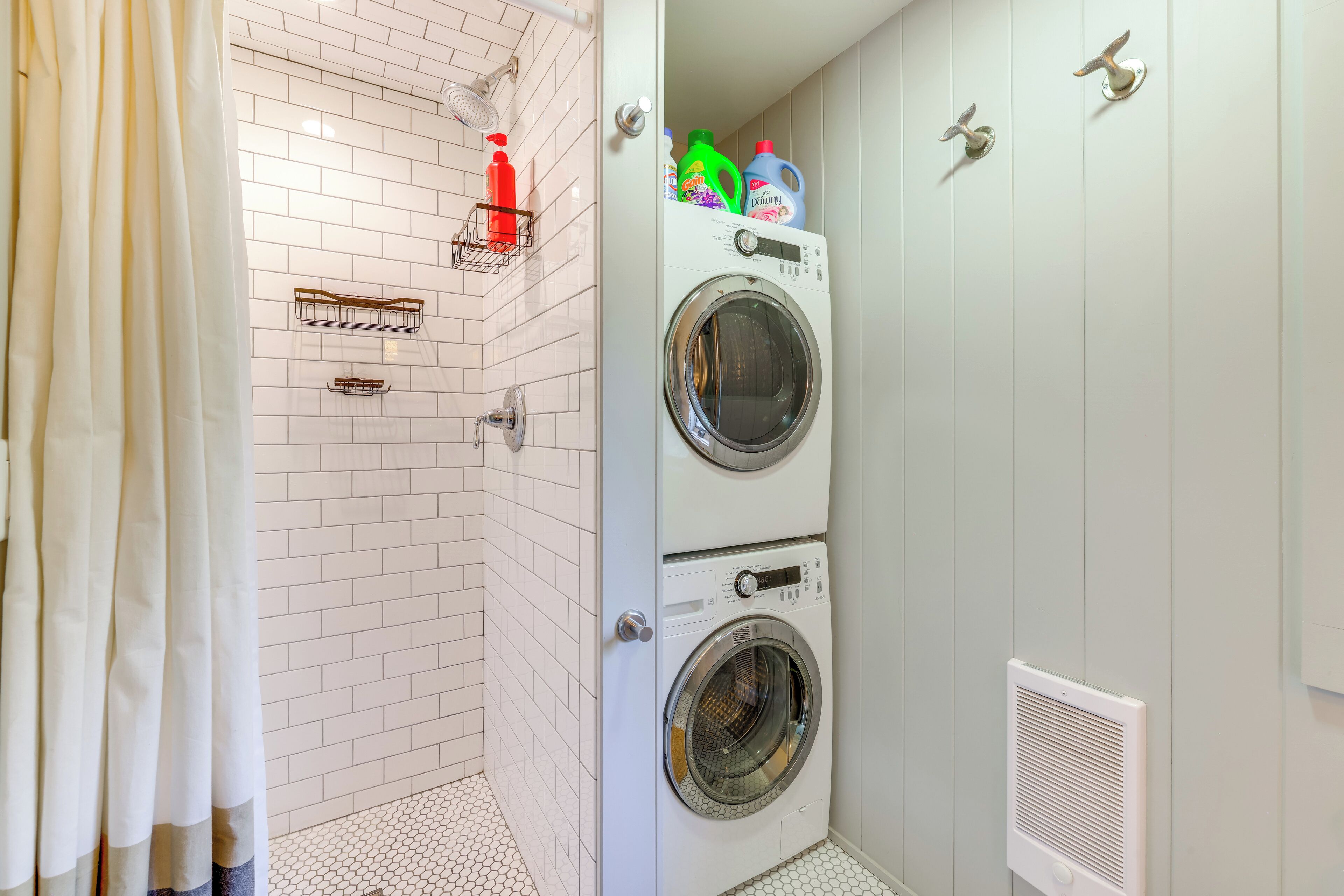 Une buanderie équipée de deux machines à laver et deux sèche-linge superposés, un espace douche avec un rideau et un sol carrelé.