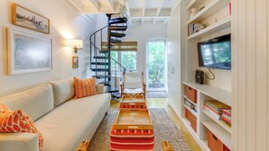 A modern living room with a white sofa, a spiral staircase, and a bookshelf. - Steps to Commercial St! Lofted Provincetown Gem (Provincetown)