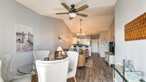 A modern kitchen with white cabinets, a dining area with a glass table, and a ceiling fan.