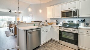 A modern kitchen with white cabinets, stainless steel appliances, and pendant lighting.