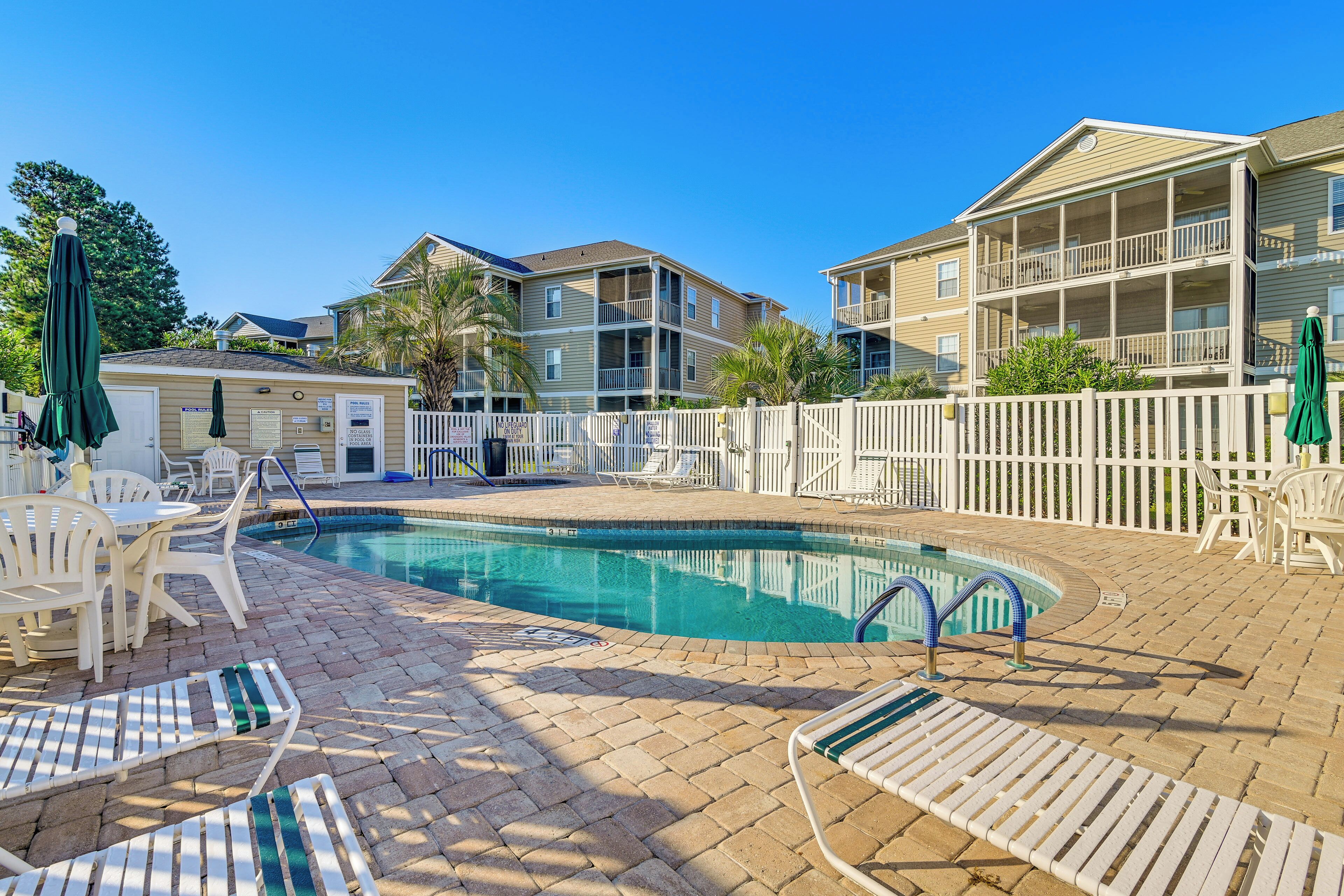 A pool area with lounge chairs, a pool, and a white fence.