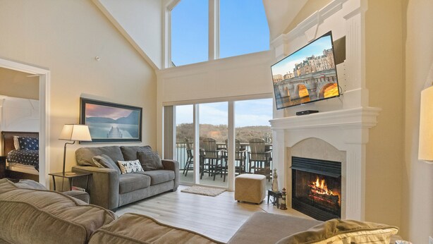 A living room with a fireplace, a sofa, a television, and a view of the outdoors. - Lakefront Camdenton Condo Near Ha Ha Tonka (Camdenton)