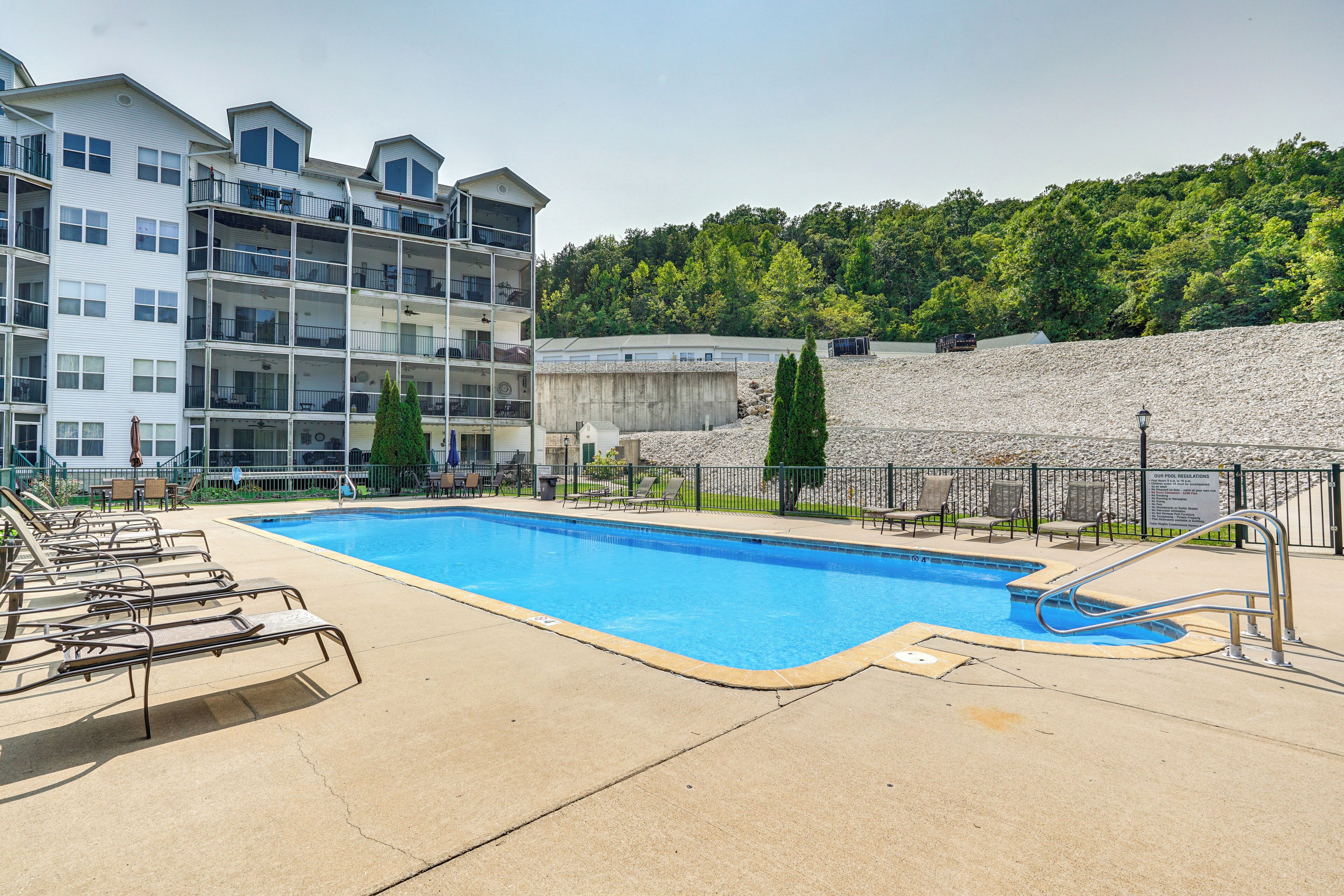 A swimming pool with lounge chairs, a concrete deck, and a multi-story building with balconies in the background.