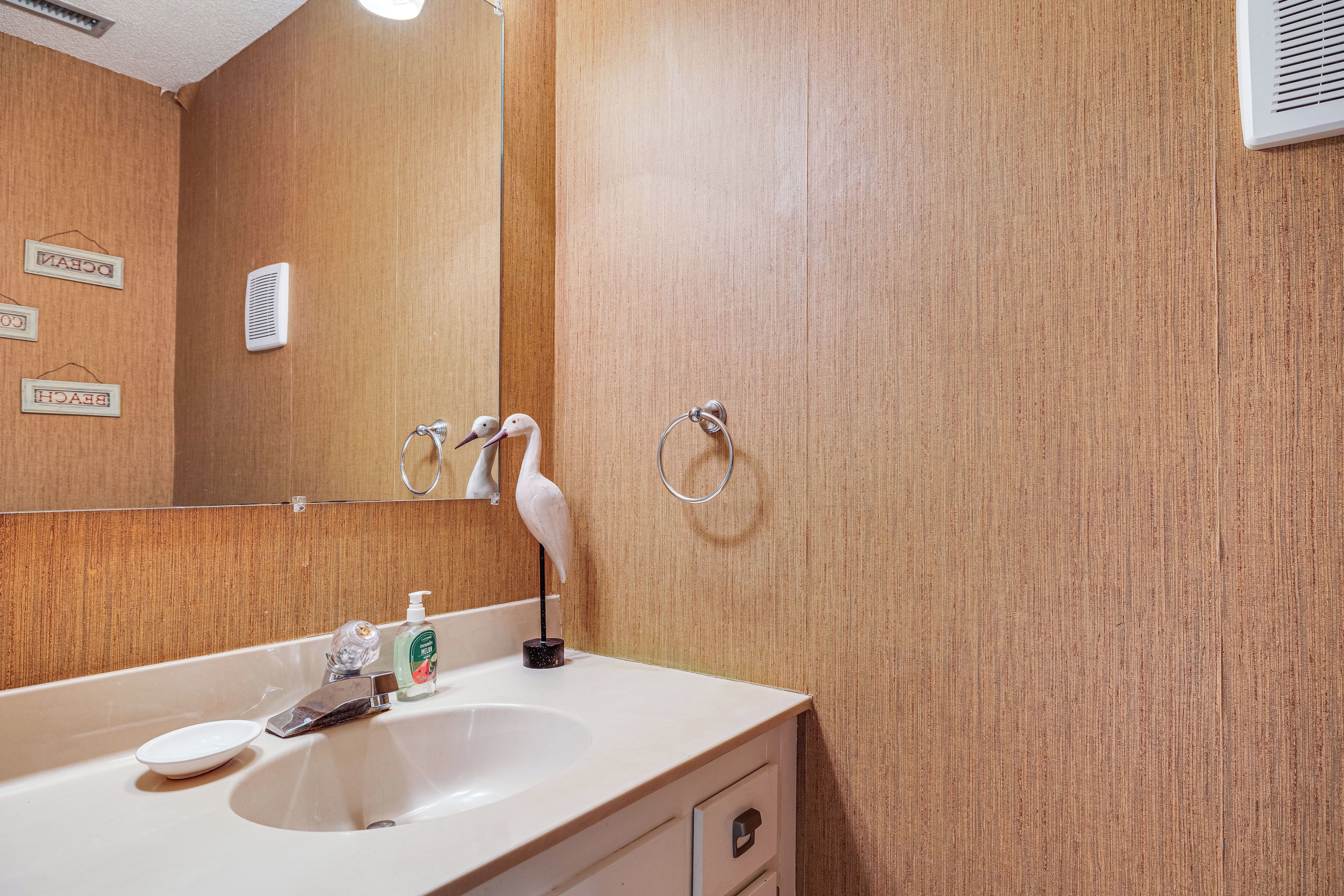 A bathroom with a wooden wall, a white sink, a mirror, and a towel ring.