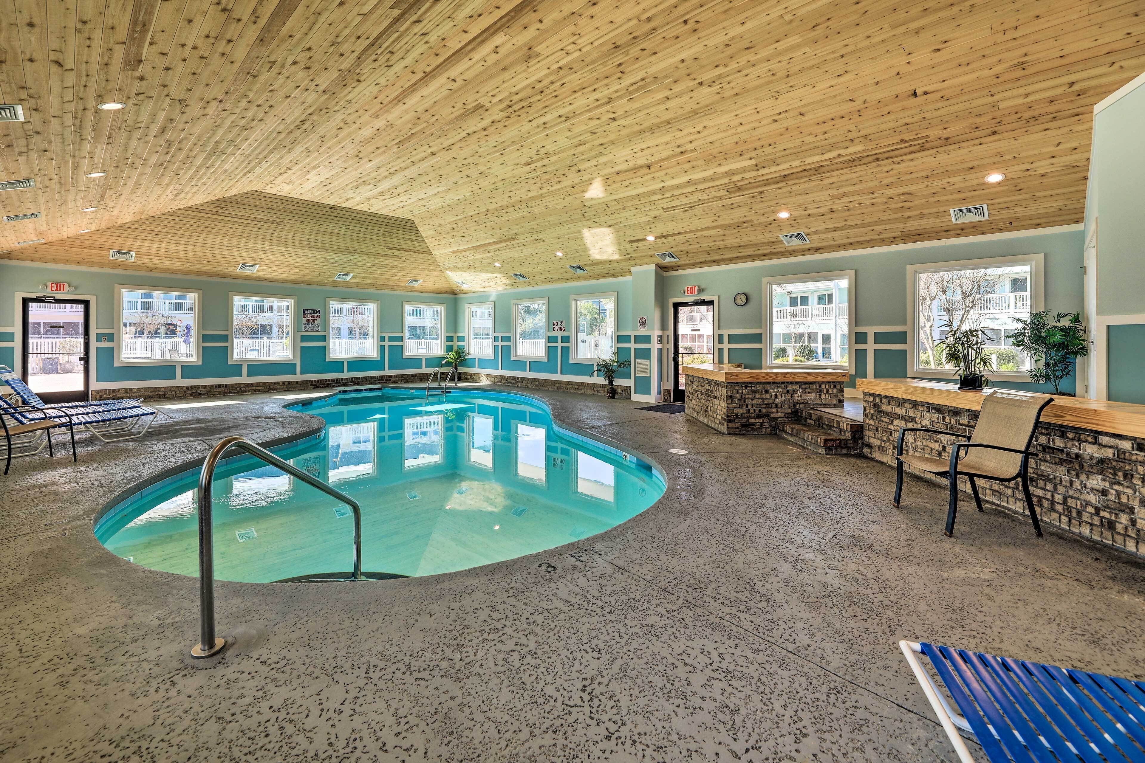 An indoor swimming pool with a wooden ceiling, a stone wall, and a seating area with chairs and a counter.