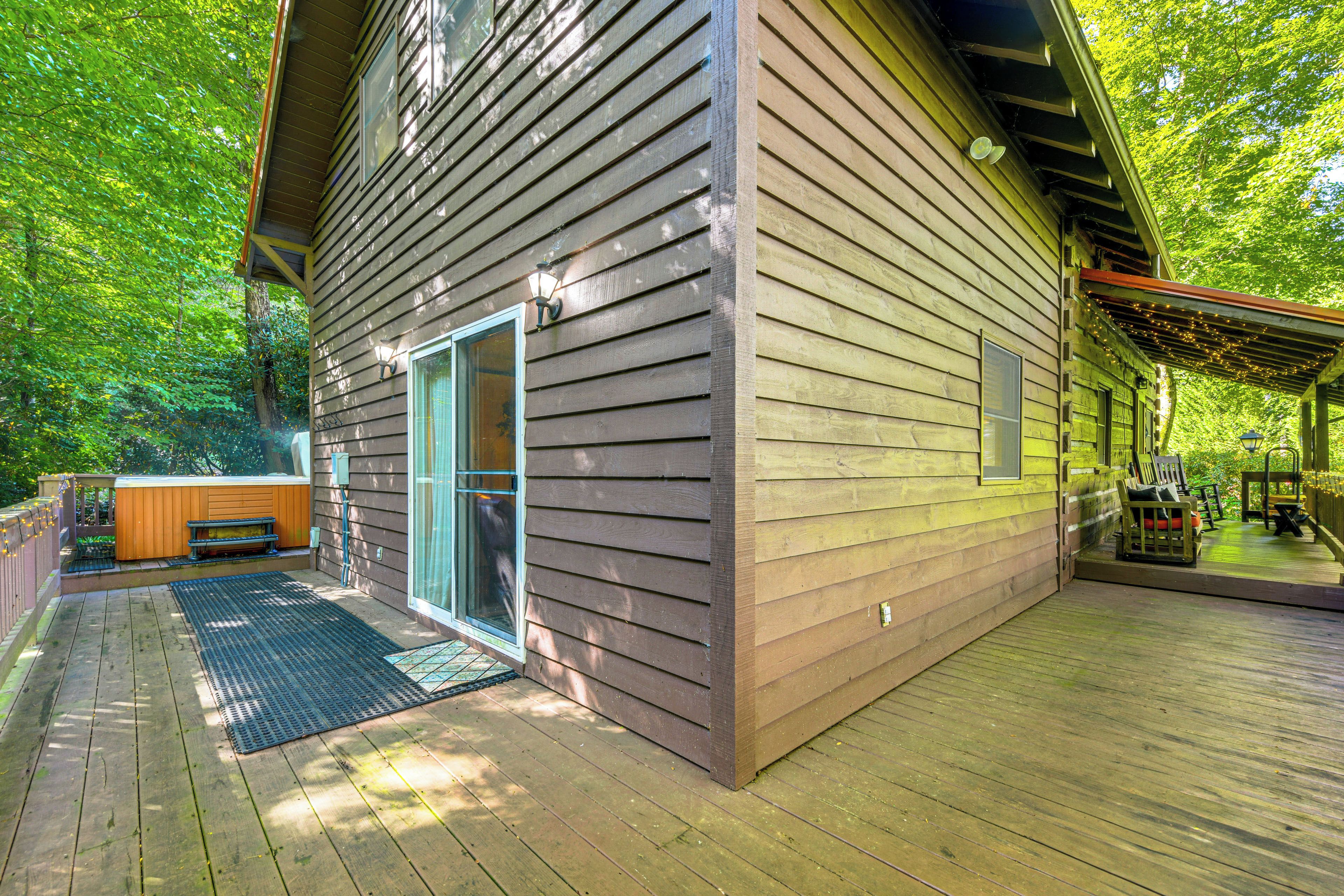 A wooden deck with a hot tub, a covered seating area, and a sliding glass door leading to a room.
