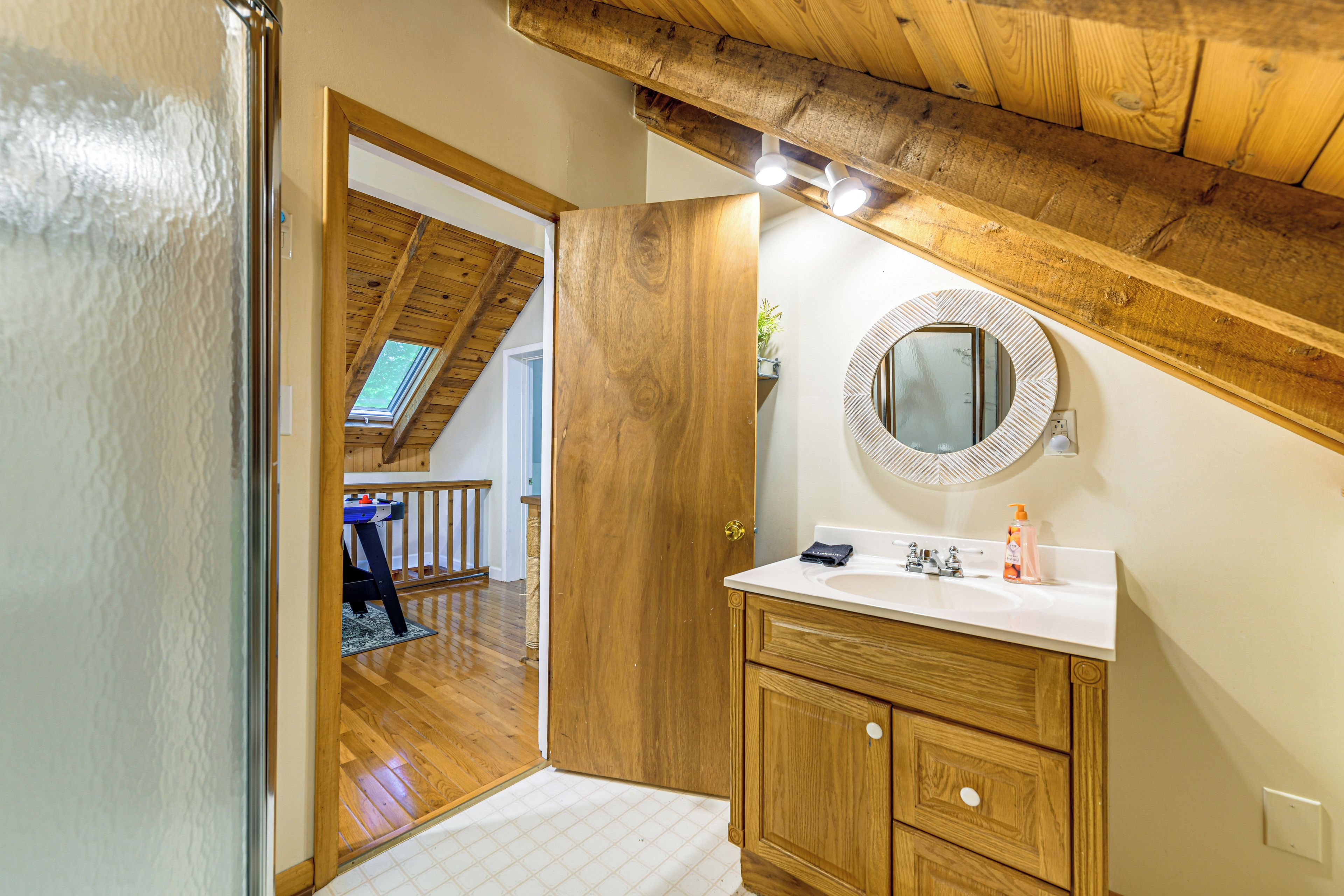 Une chambre mansardée avec une structure en bois, dotée d’une coiffeuse blanche, d’un miroir rond et offrant une vue sur le balcon.