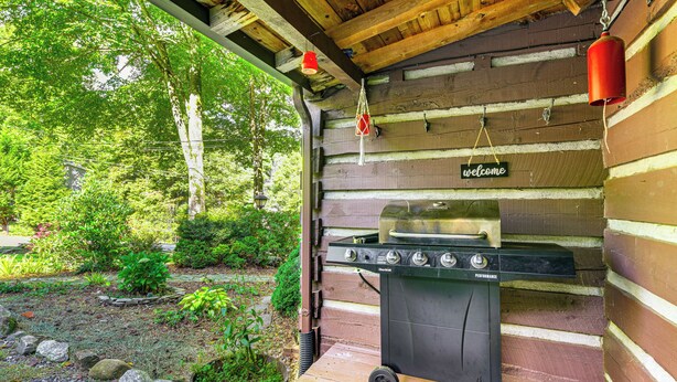 A wooden cabin with a barbecue grill, a welcome sign, and a red lantern. - Hot Tub & Fire Pit: Cozy Cabin in Maggie Valley (Maggie Valley)