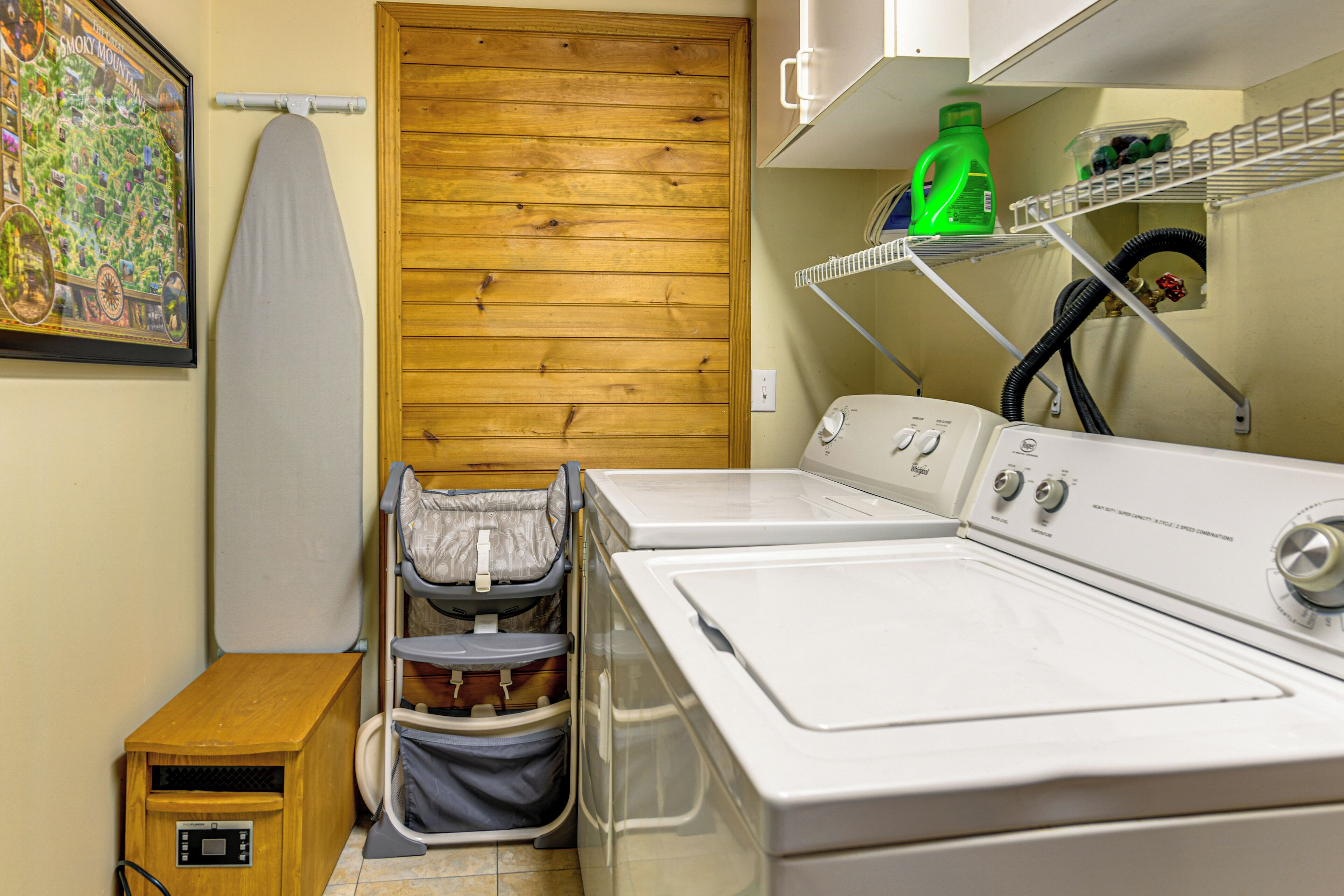 A laundry area with two washing machines, a drying rack, and a small wooden cabinet.