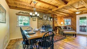 Un coin repas avec une table et des chaises en bois, une cheminée en pierre et une vue sur l’extérieur grâce à de grandes fenêtres.