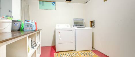 A laundry room with a red floor, white washing machines, and shelves with cleaning supplies.