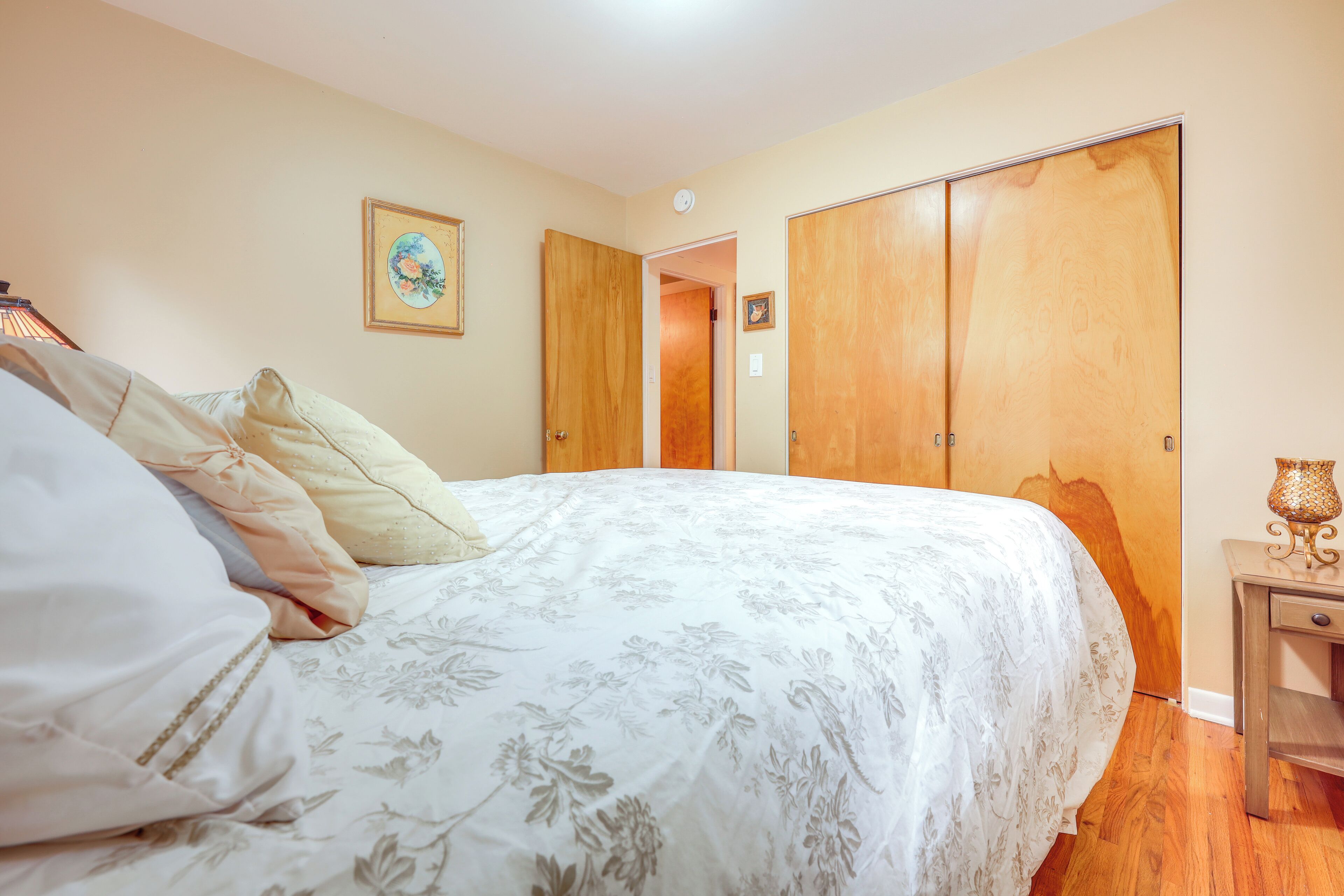 A bedroom with a bed, a wooden wardrobe, and a nightstand with a lamp.