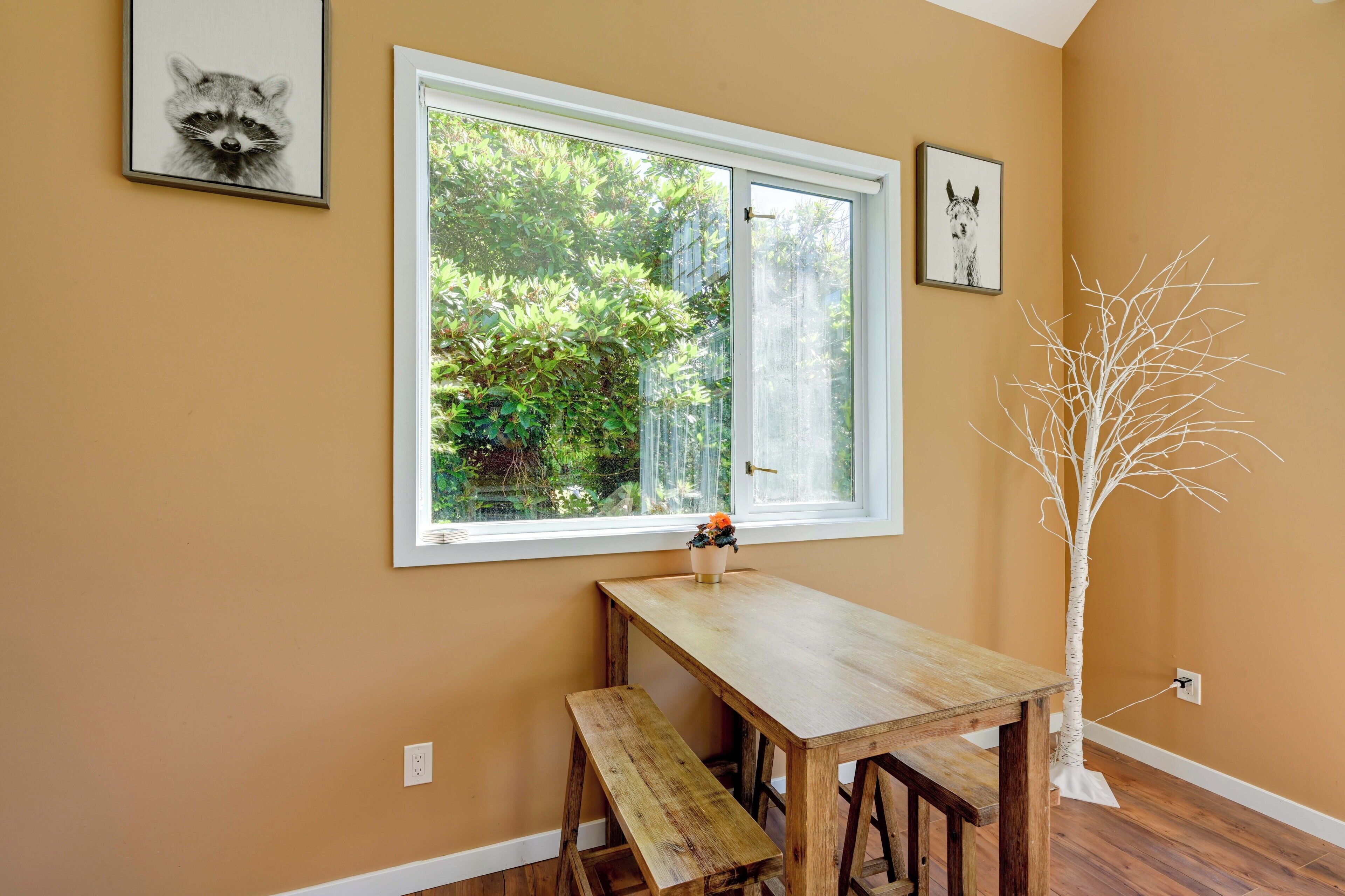 Una habitación con ventana, una mesa de madera, un banco y una escultura blanca con forma de árbol.