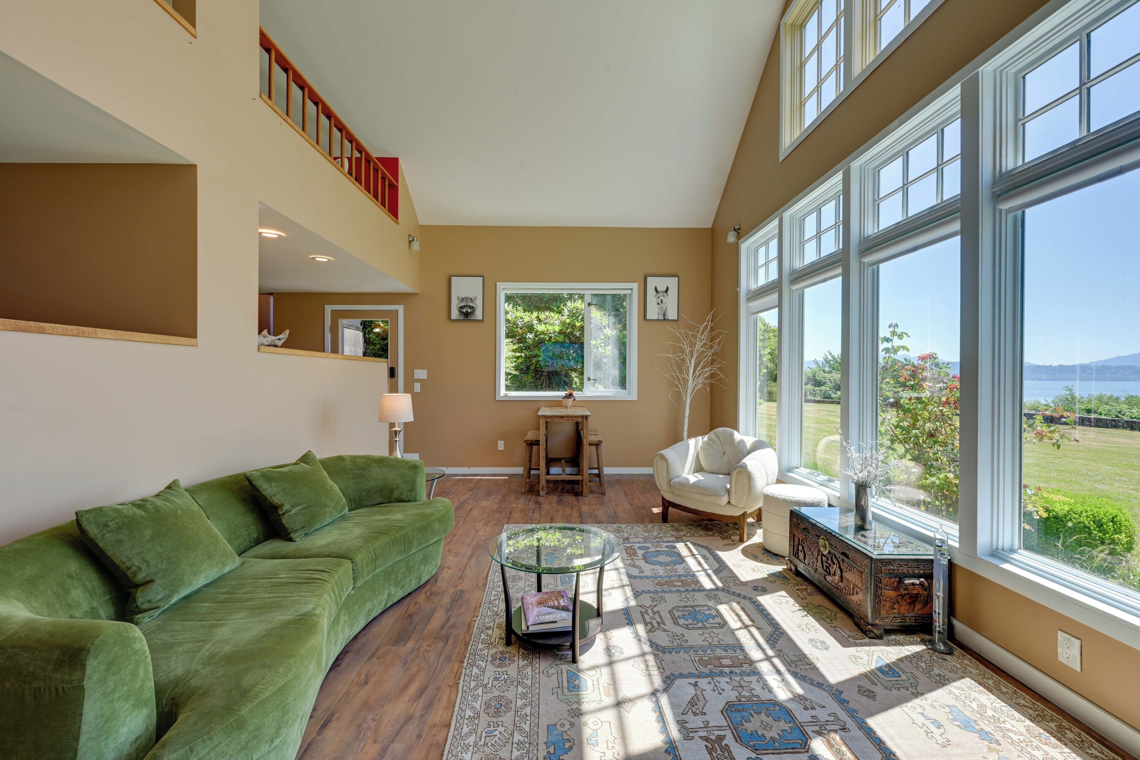 A spacious living room with a green sofa, a glass coffee table, and a view of a garden through large windows.