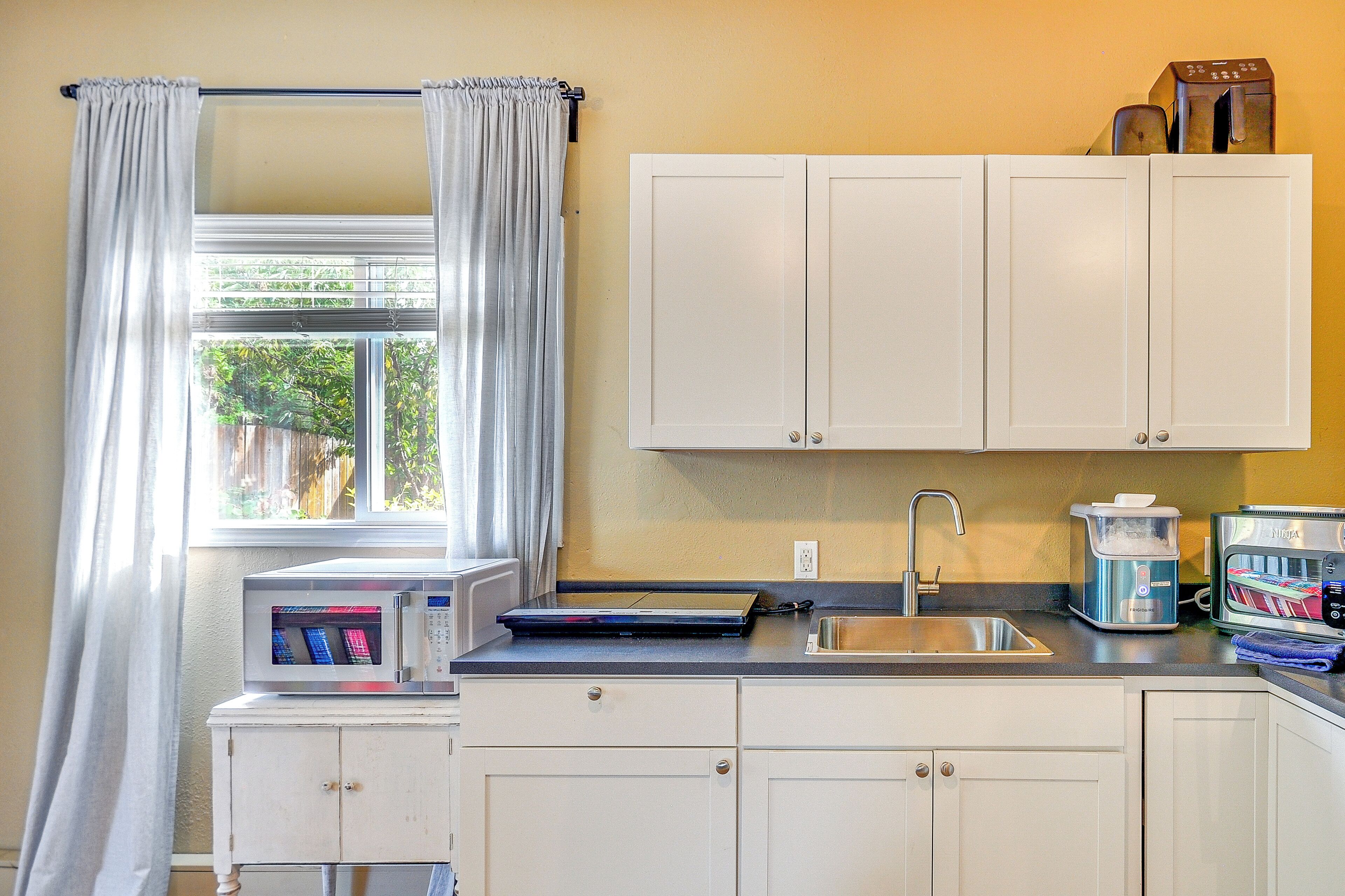 A compact kitchen with white cabinets, a microwave, a toaster, and a sink.