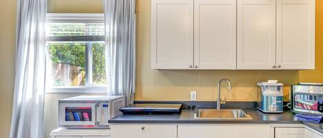 A compact kitchen with white cabinets, a microwave, a toaster, and a sink.