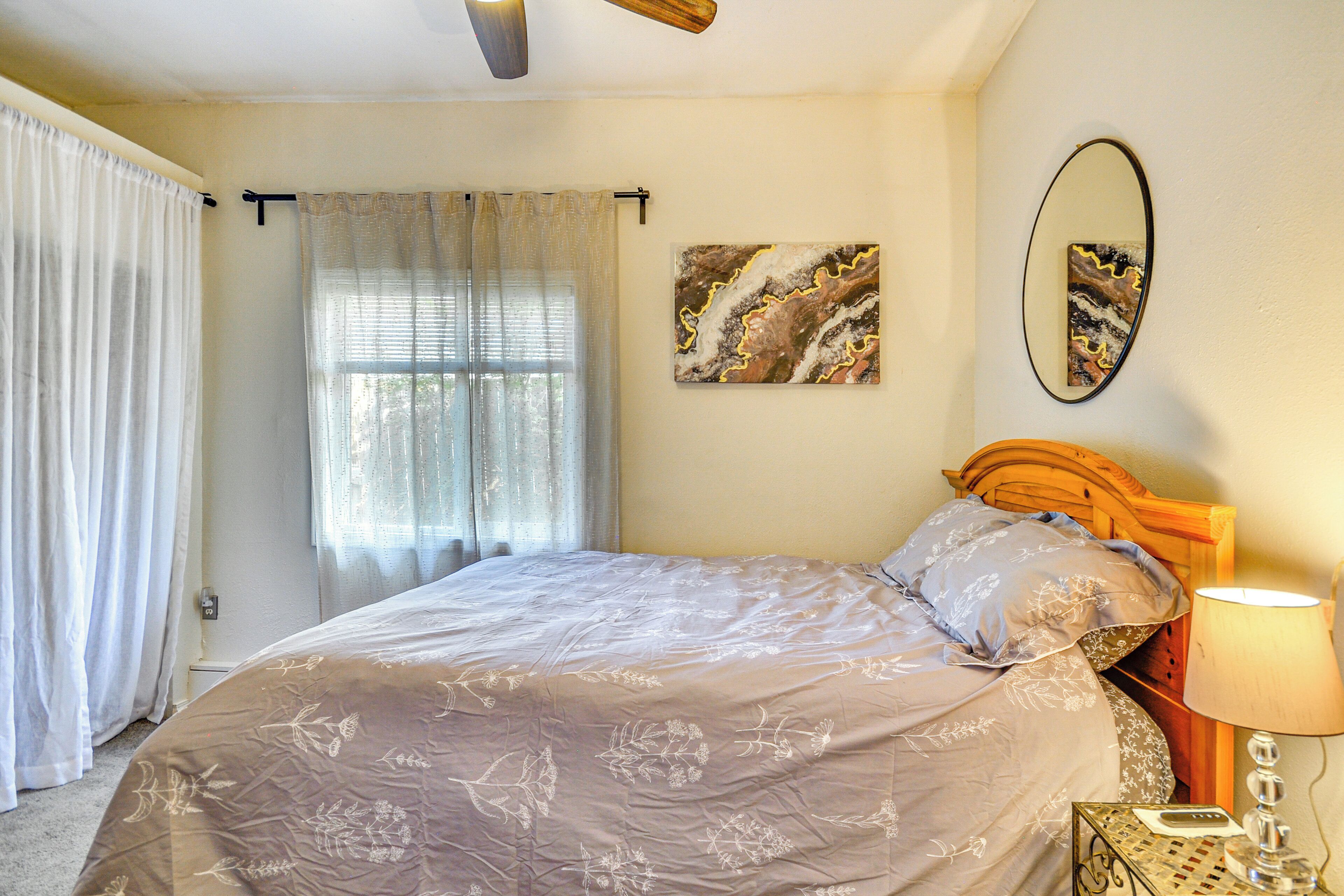 Une chambre à coucher avec un lit, des rideaux, une fenêtre, un miroir fixé au mur et une table de chevet avec une lampe.