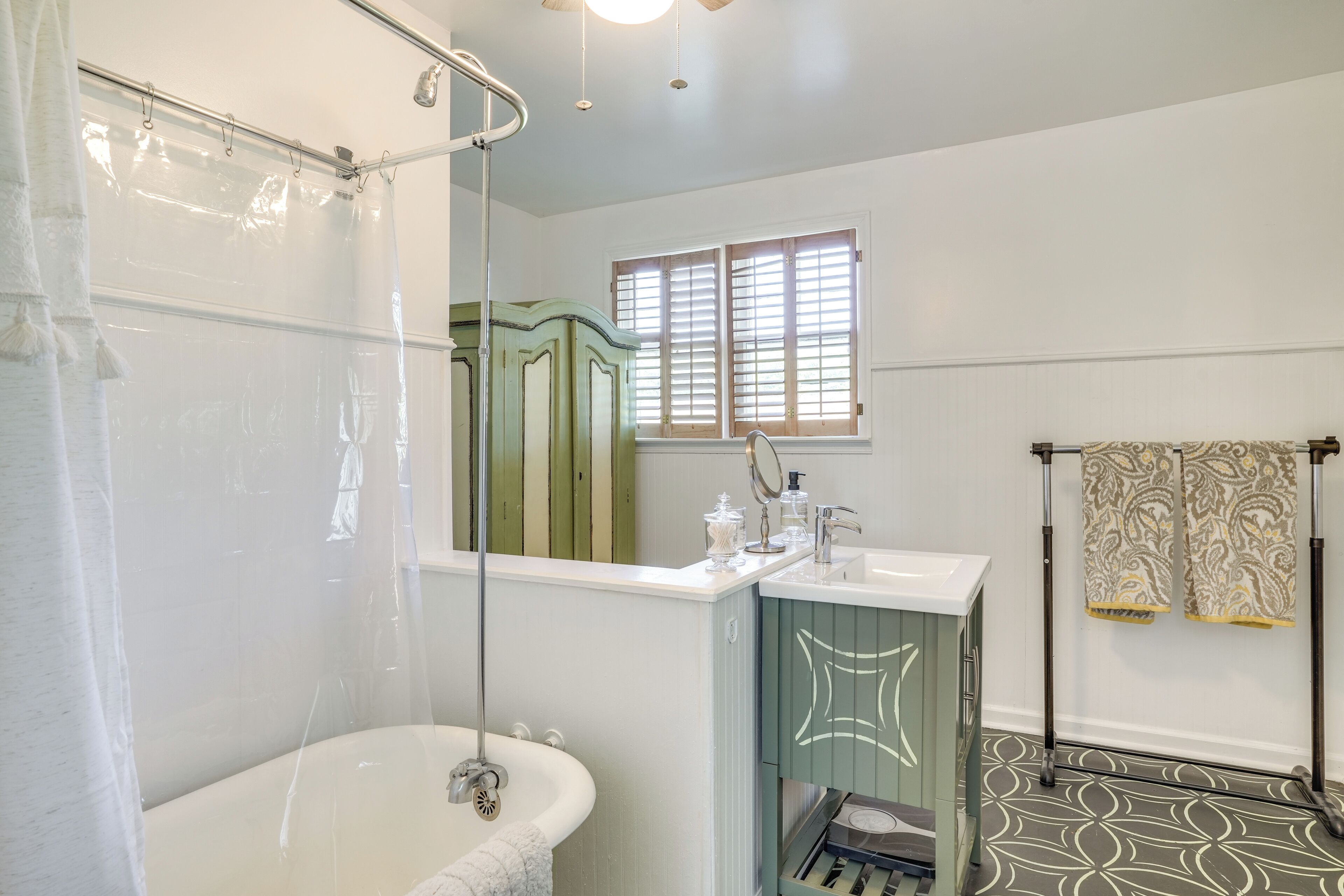 A bathroom with a bathtub, a sink, a vanity with a mirror, and a window with blinds.