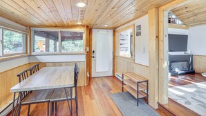 Un interior de madera con una mesa de comedor, sillas, un banco, una chimenea y ventanas amplias.