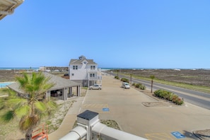 A coastal building with a parking lot, a palm tree, and a clear sky. - Walk to Beach: Corpus Christi Gem on Padre Island! (Corpus Christi)