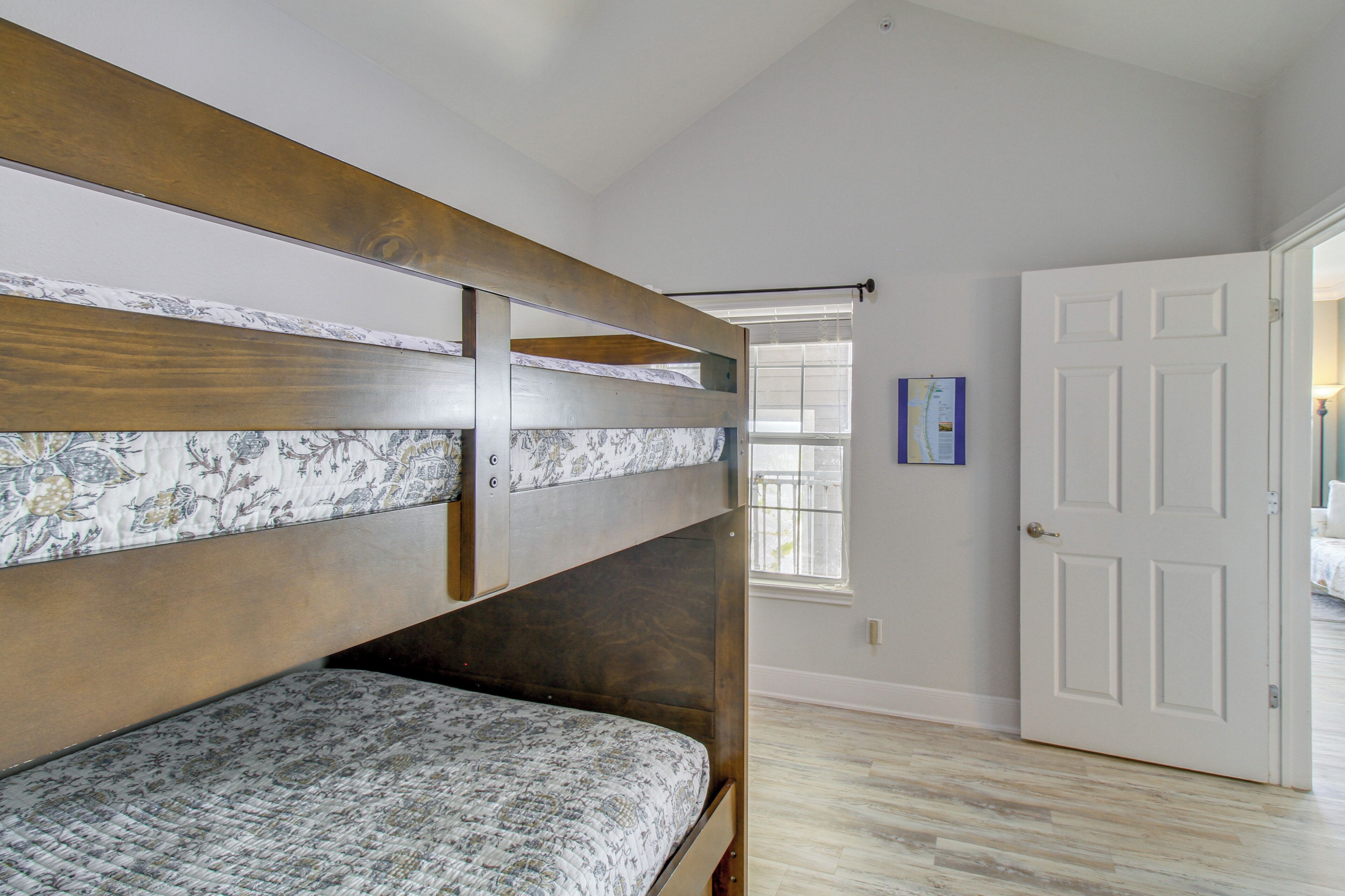 A bunk bed with patterned bedding, a white door, and a window with blinds.