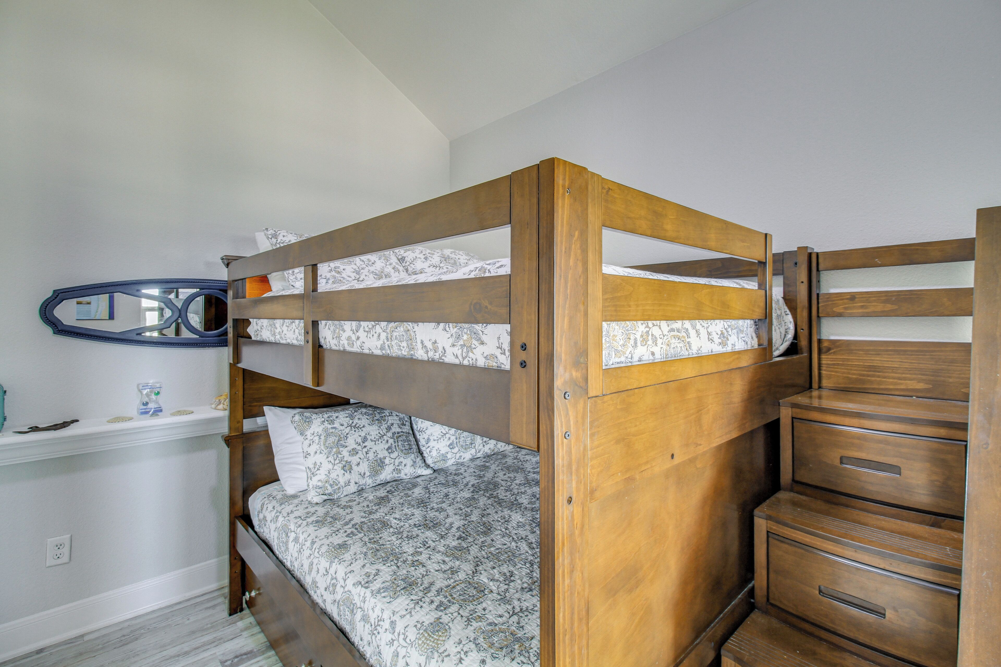 A bunk bed with a wooden frame, a bedside table, and a mirror on the wall.