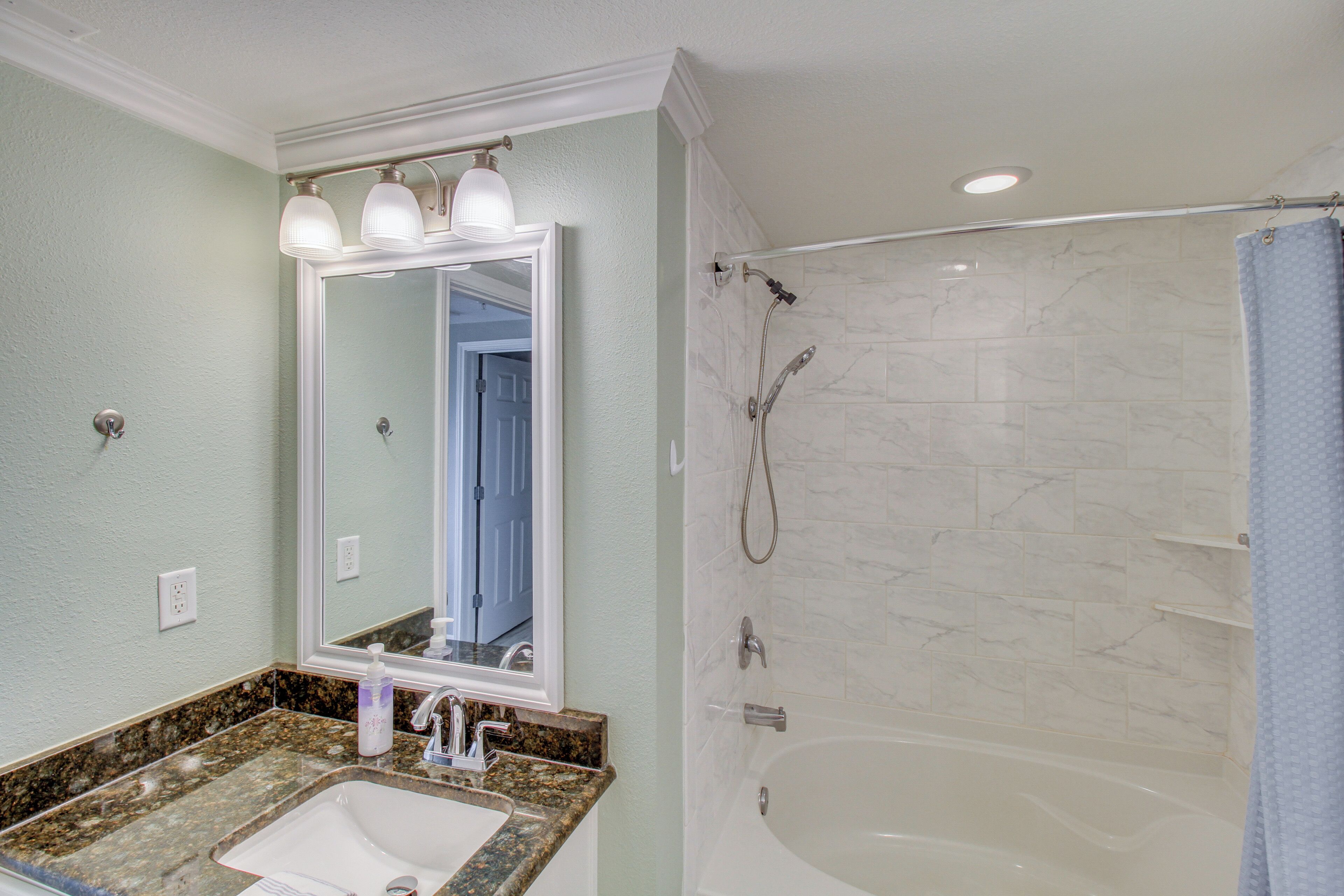 Un bagno con lavandino, specchio, doccia e portasciugamani.