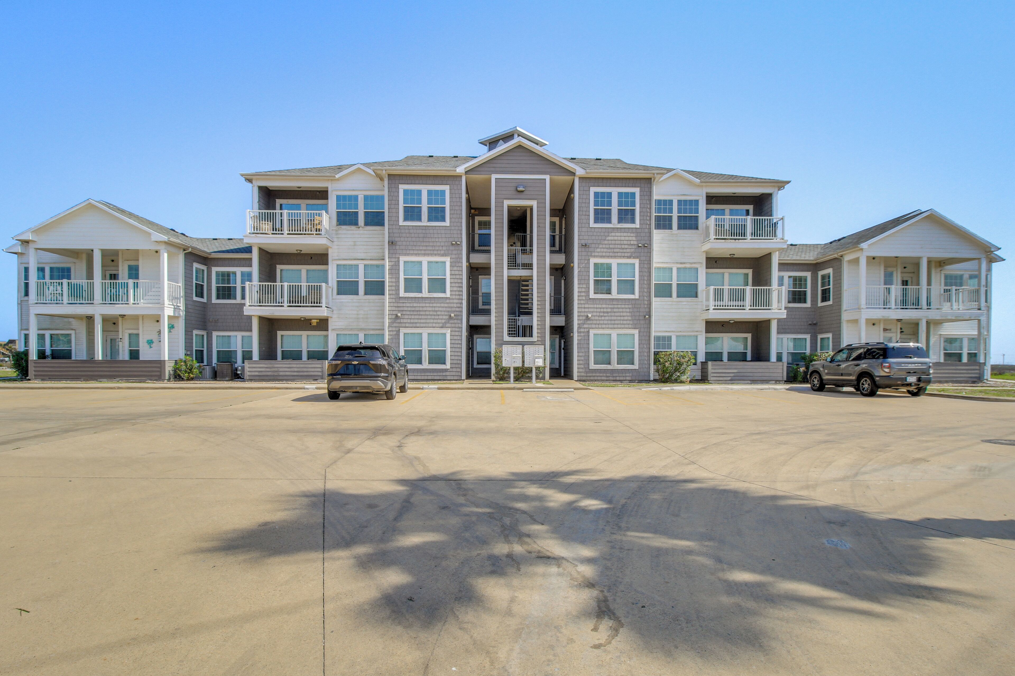 A multi-story residential building with a central entrance, balconies, and a parking area.