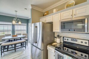 Una cocina moderna con electrodomésticos de acero inoxidable, un comedor con banco y vistas amplias a través de grandes ventanales.