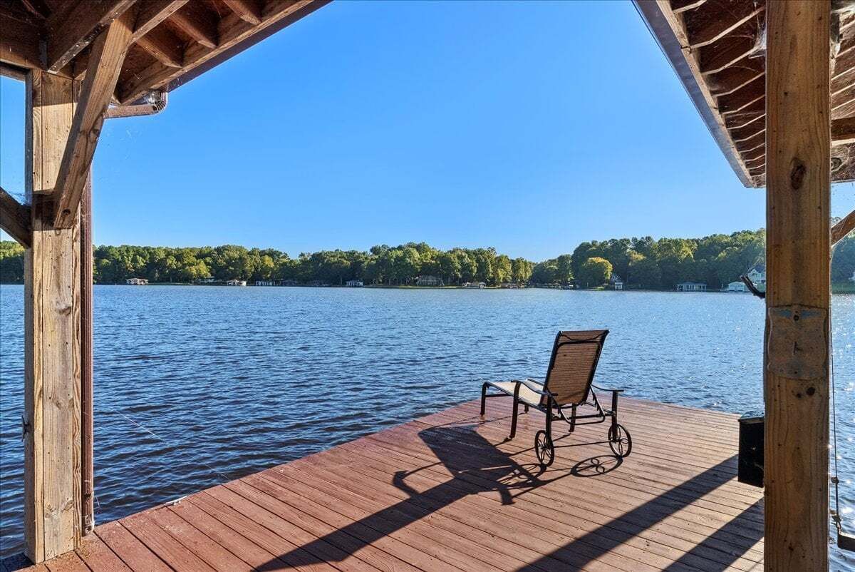 Terraza de madera con una sola silla que da a un lago tranquilo y una orilla boscosa.