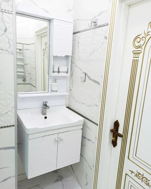 A bathroom with a white vanity, a mirror, and a door with gold detailing.