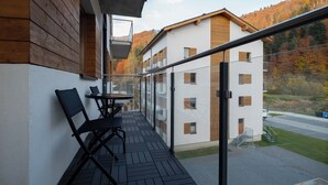 A balcony with a table and chairs, overlooking a residential area with autumn-colored trees and a building with wooden accents. - Apartamenty Sun & Snow River Park (Wisla)