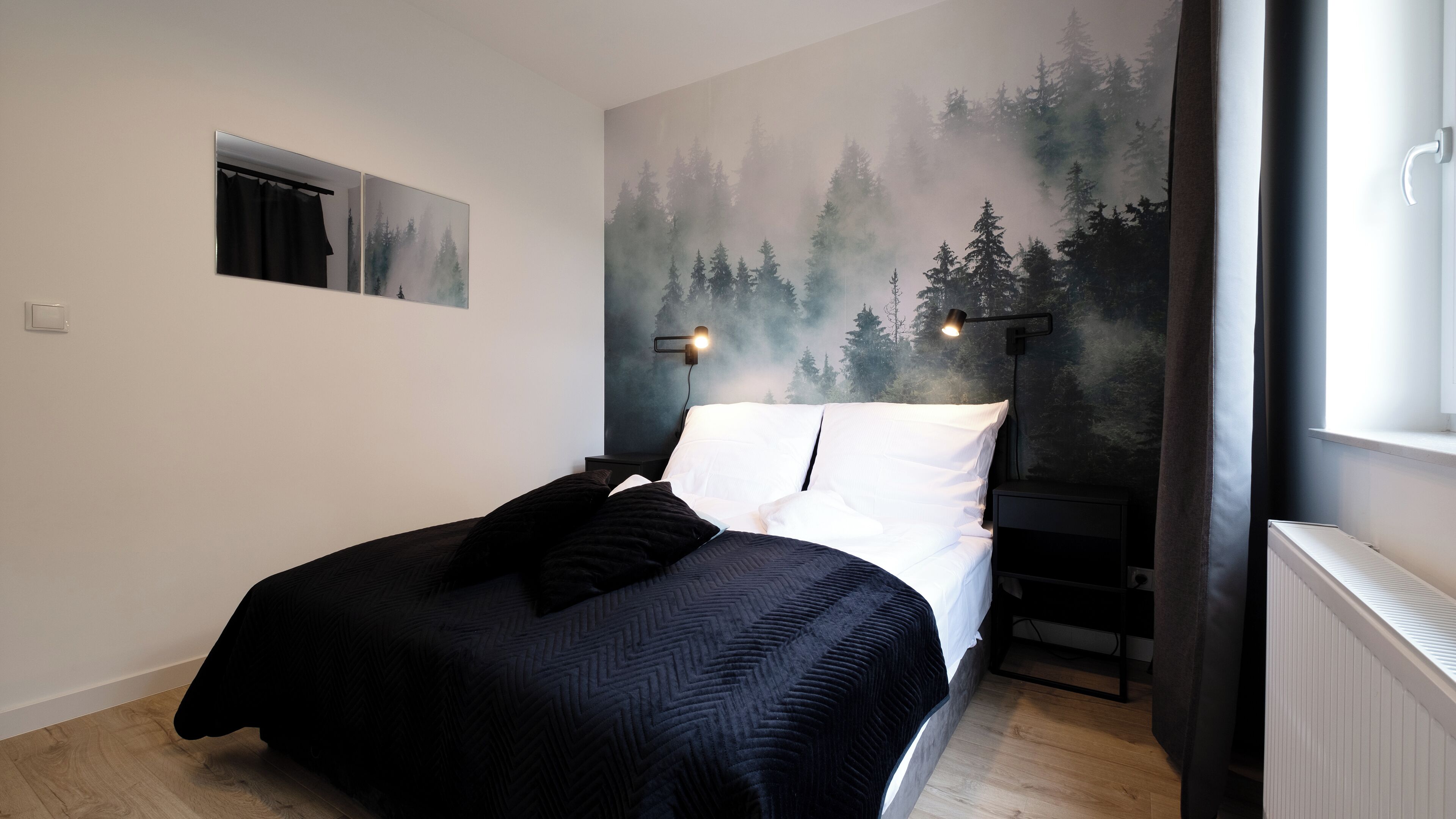 A bedroom with a bed, a nightstand, a wall-mounted lamp, and a window with curtains.