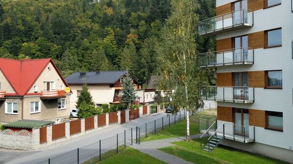 A residential area with modern houses, a fenced pathway, and a backdrop of dense forest. - Apartamenty Sun & Snow River Park (Wisla)