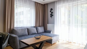 A modern living room with a grey sofa, a wooden coffee table, sheer curtains, and a decorative wall piece. - Apartamenty Sun & Snow River Park (Wisla)