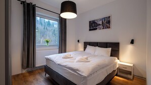 A bedroom with a large bed, a window with curtains, a painting on the wall, and a bedside table with a lamp. - Apartamenty Sun & Snow River Park (Wisla)