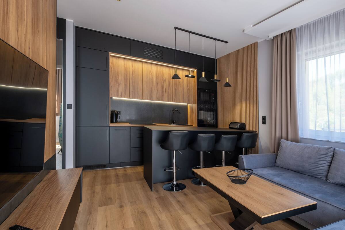 A modern kitchen with a wooden countertop, black bar stools, and a built-in oven.