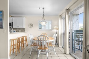 Un coin repas avec une table ronde, des chaises en bois, un luminaire suspendu, une horloge et une vue à travers une porte vitrée.