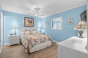 Une chambre à coucher comprenant un lit, des tables de chevet, un ventilateur de plafond et des œuvres d’art murales.