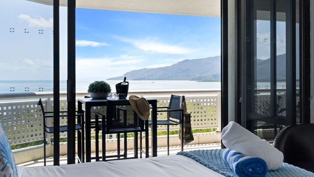Un balcón con una cama, una mesa con una planta y vistas al mar y las montañas.