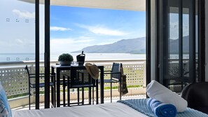 Un balcón con una cama, una mesa con una planta y vistas al mar y las montañas.