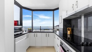 Una cocina moderna con armarios blancos, encimera negra y vistas al mar a través de amplios ventanales.