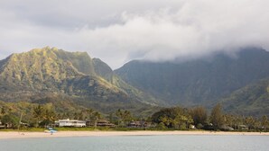 A beach with a mountain in the background, houses along the shore, and a clear sky. - The Cliffs Condos (Princeville)