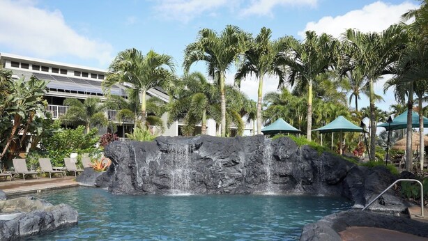 A pool with a waterfall feature, surrounded by palm trees and lounge chairs. - The Cliffs Condos (Princeville)