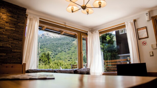 A room with a large window offering a mountain view, a wooden ceiling, and a chandelier. - Apartamentos Catedral inn (San Carlos de Bariloche)