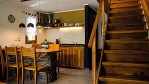 A kitchen with wooden cabinets, a dining table with chairs, a wooden staircase, and pendant lighting. - Apartamentos Catedral inn (San Carlos de Bariloche)